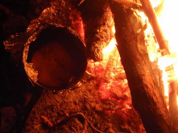 Damper bread bakes in the coals on a fire