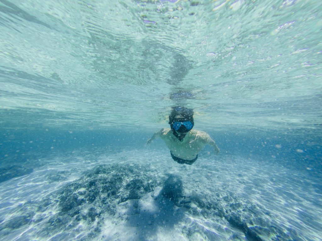 A male snorkler swims towards the camera in light blue water