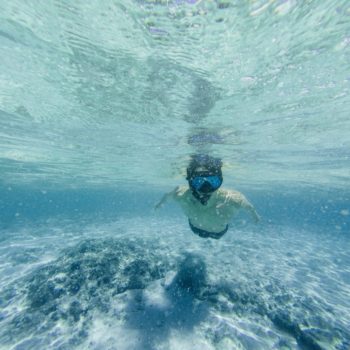 A male snorkler swims towards the camera in light blue water