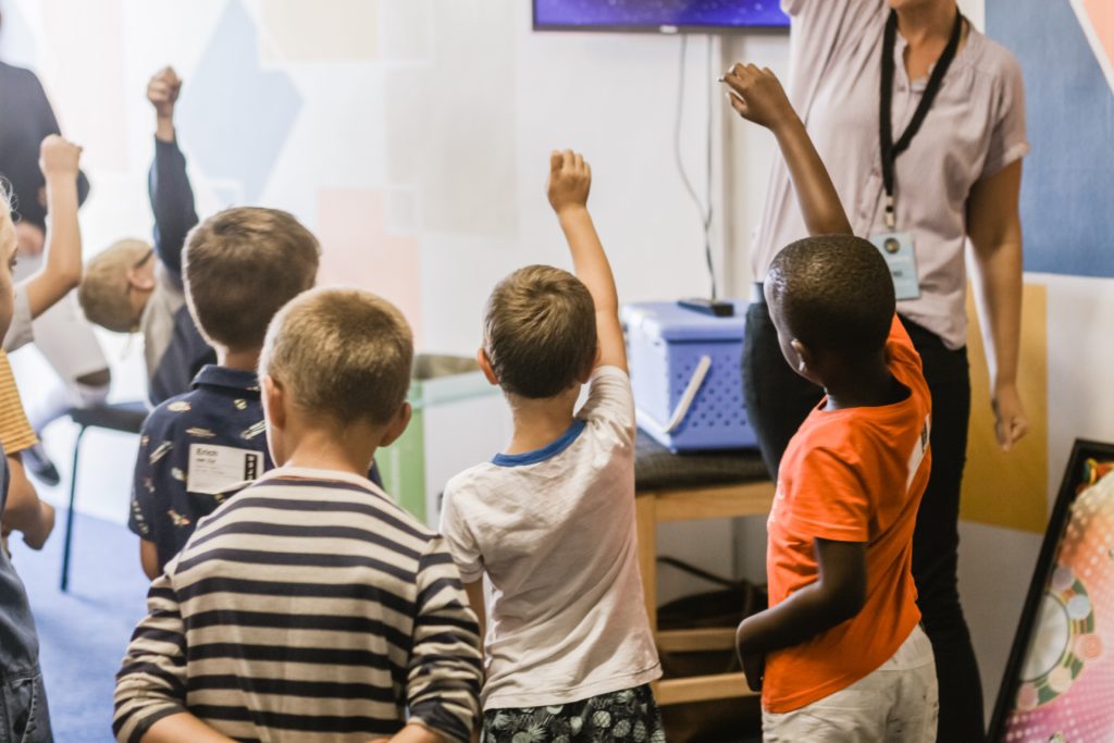 Several students raise their hands as they look at a whiteboard